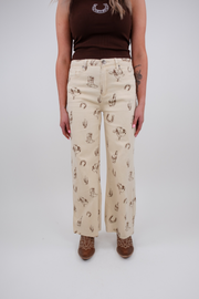 Person wearing beige pants with horse print and brown top on a white background