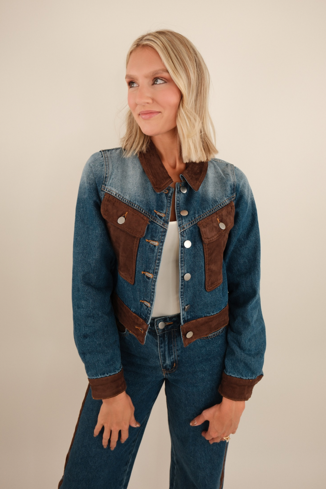 Medium-wash cropped denim jacket with brown suede contrast panels on collar, chest pockets, hem, and cuffs, western-inspired style.