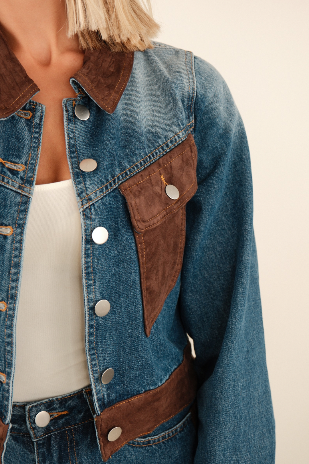 Close-up of cropped denim jacket highlighting suede collar and chest pocket details with contrast stitching.