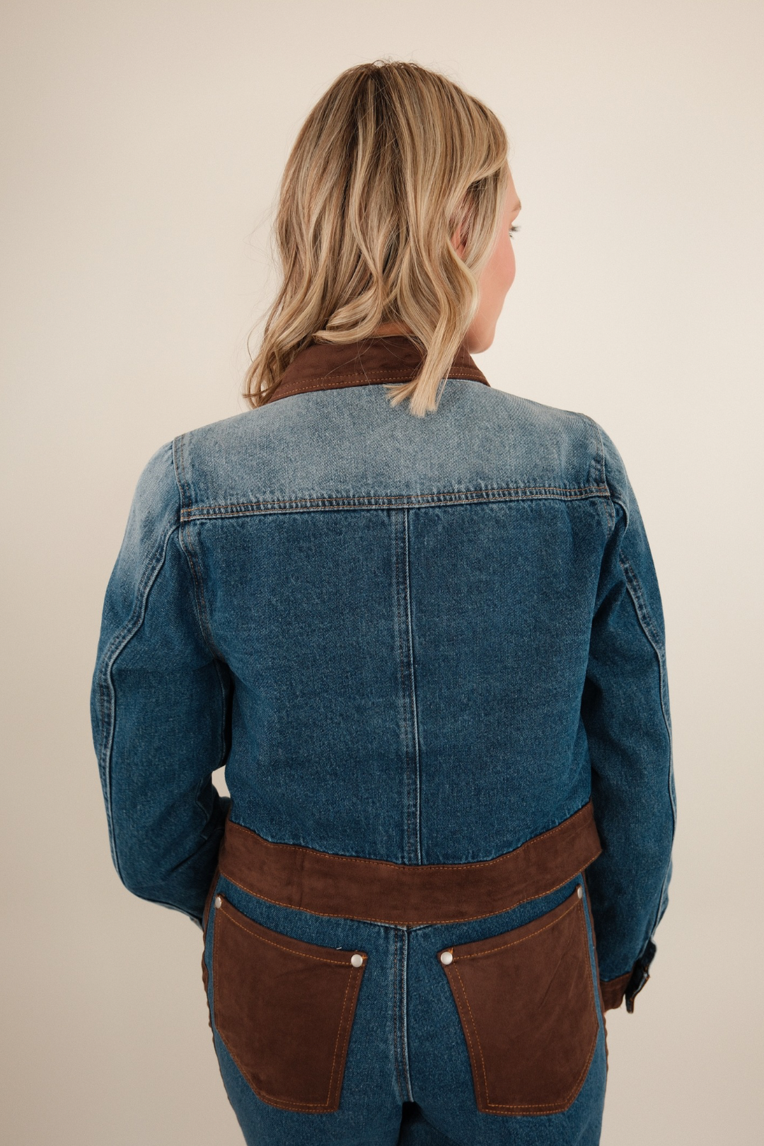 Back of cropped denim jacket featuring denim body with suede accents on hem and cuffs.