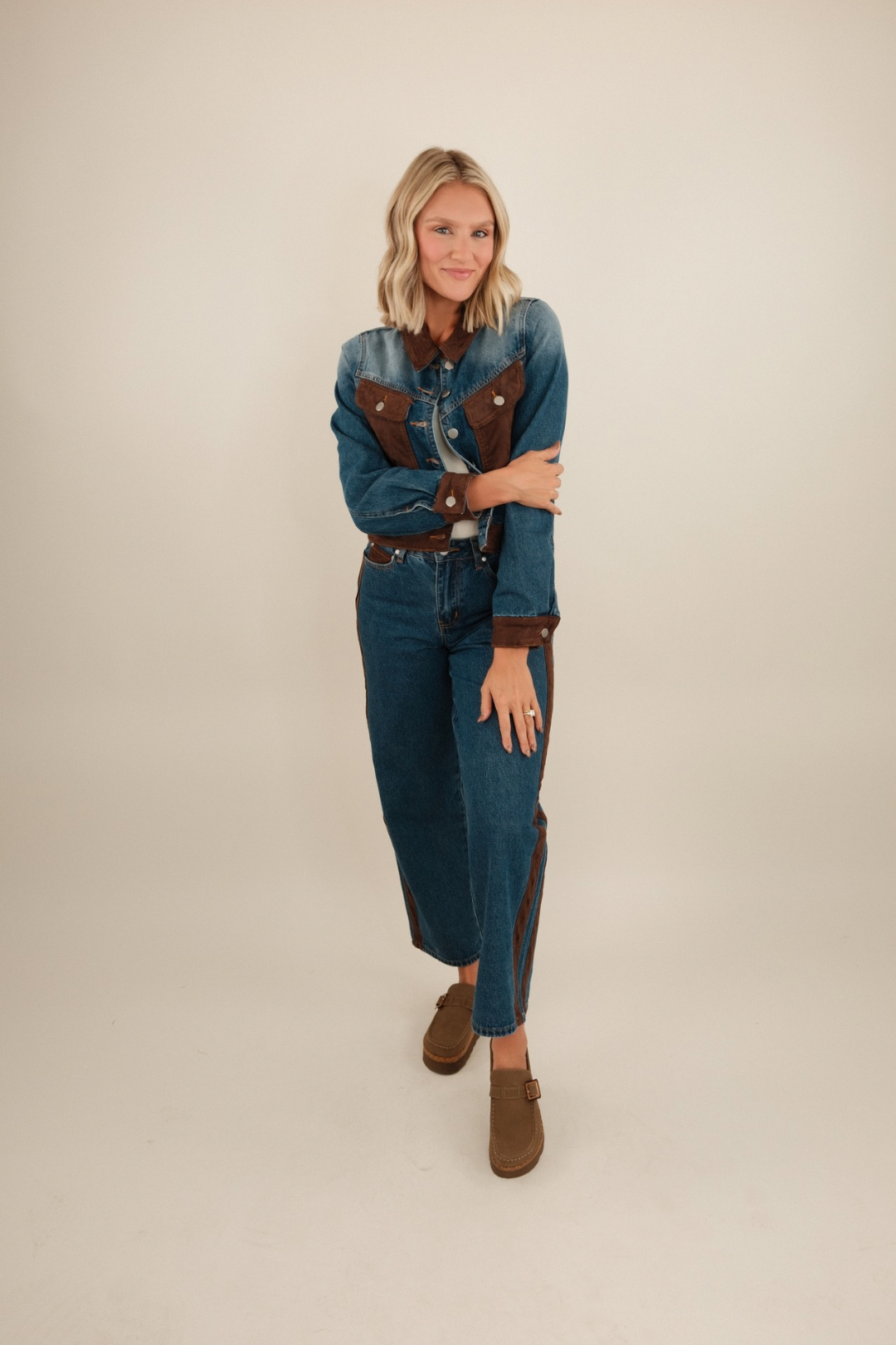 Model wearing cropped denim jacket with suede collar, chest pockets, cuffs, and hem, styled in a western-inspired look.