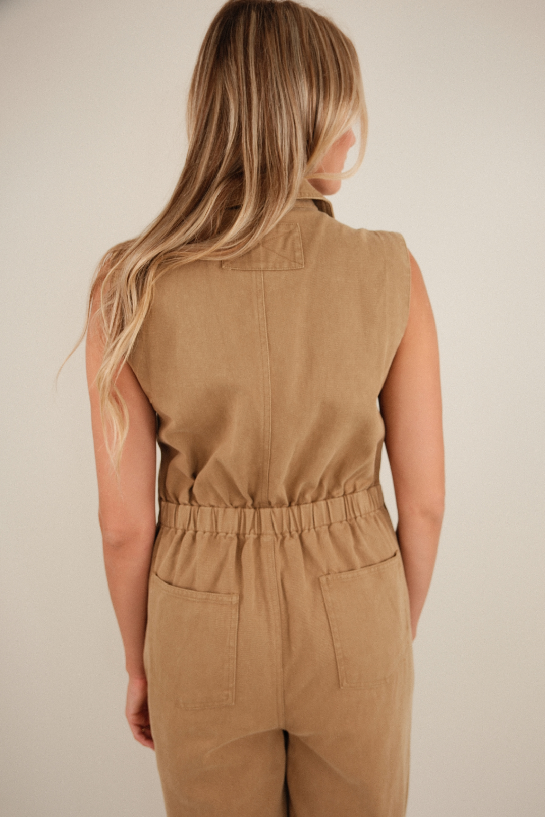 Woman wearing a beige sleeveless jumpsuit against a plain background