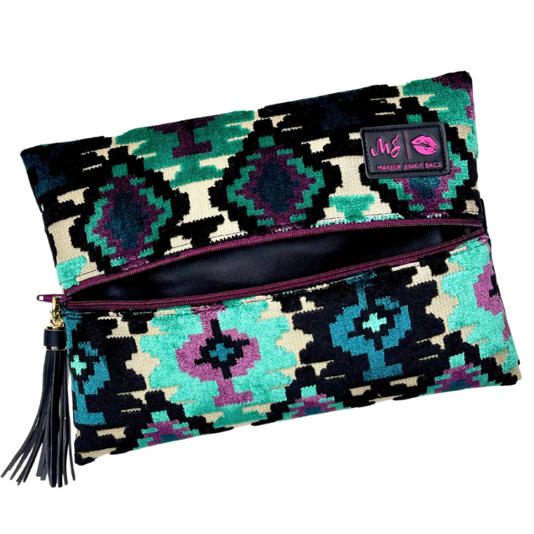 Front view of Aztec Emerald Makeup Junkie bag in teal velvet with bold Aztec-print exterior, purple zipper and branded tassel accent.