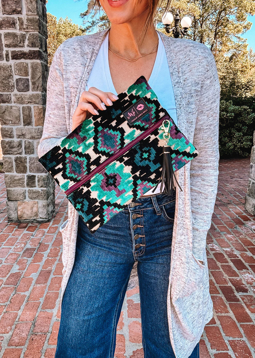 Person holding the Aztec Emerald Makeup Junkie travel bag with teal Aztec pattern, purple zipper, and tassel, highlighting its compact design