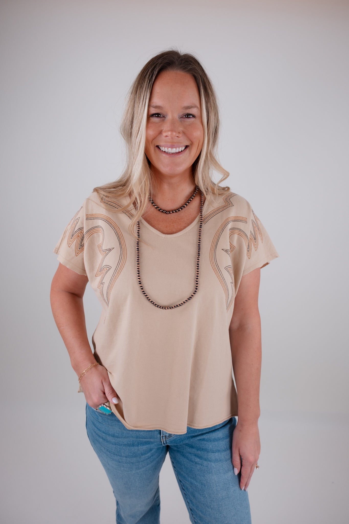 Woman wearing a beige blouse with boot stitch sleeves and blue jeans against a plain background