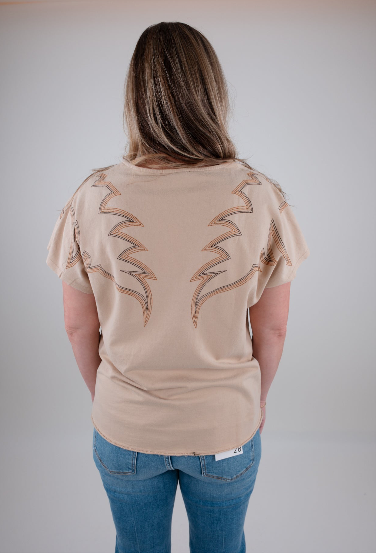 Person wearing a beige t-shirt with a unique design on the back against a plain background