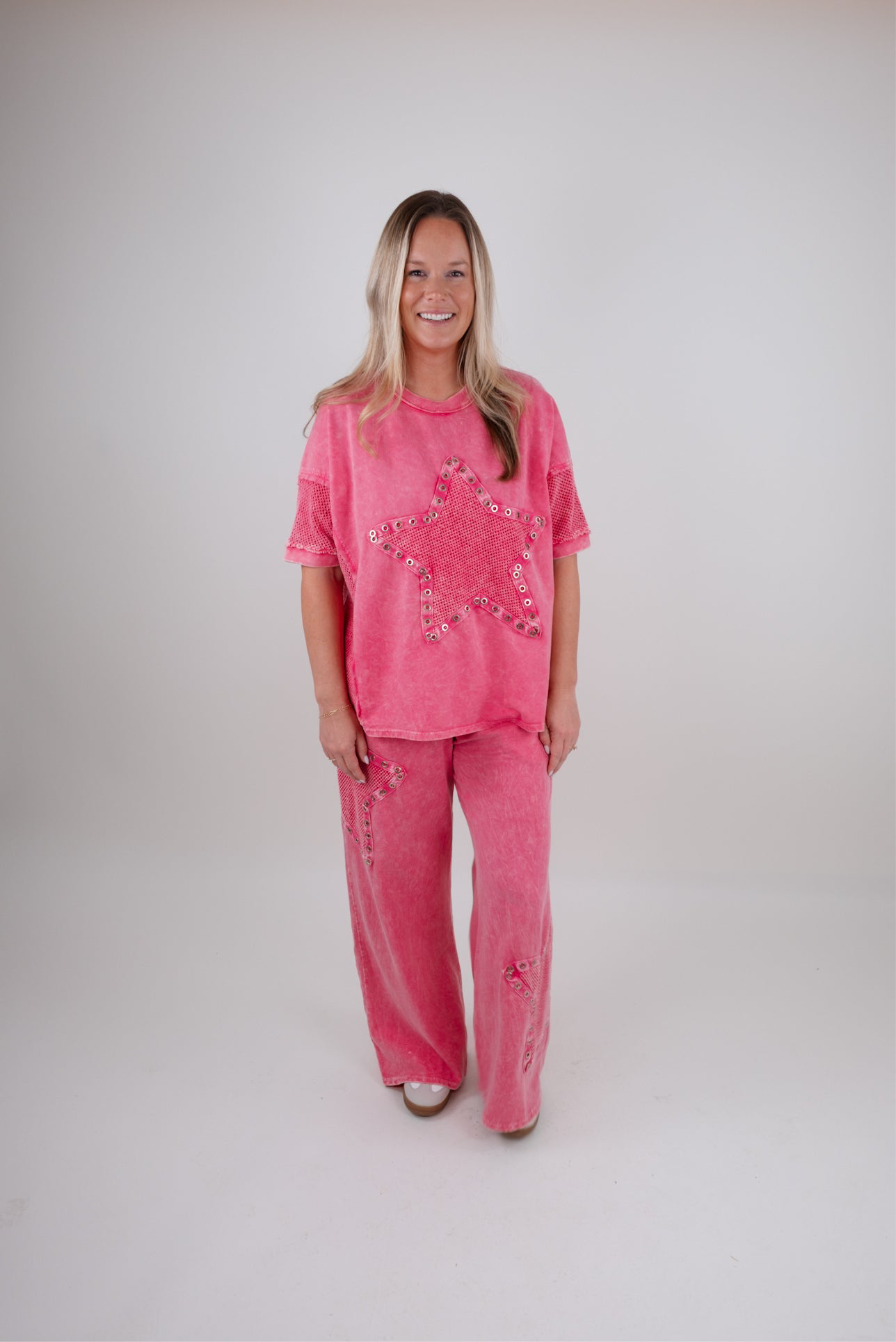 Woman wearing a pink outfit with star embellishments on a plain background
