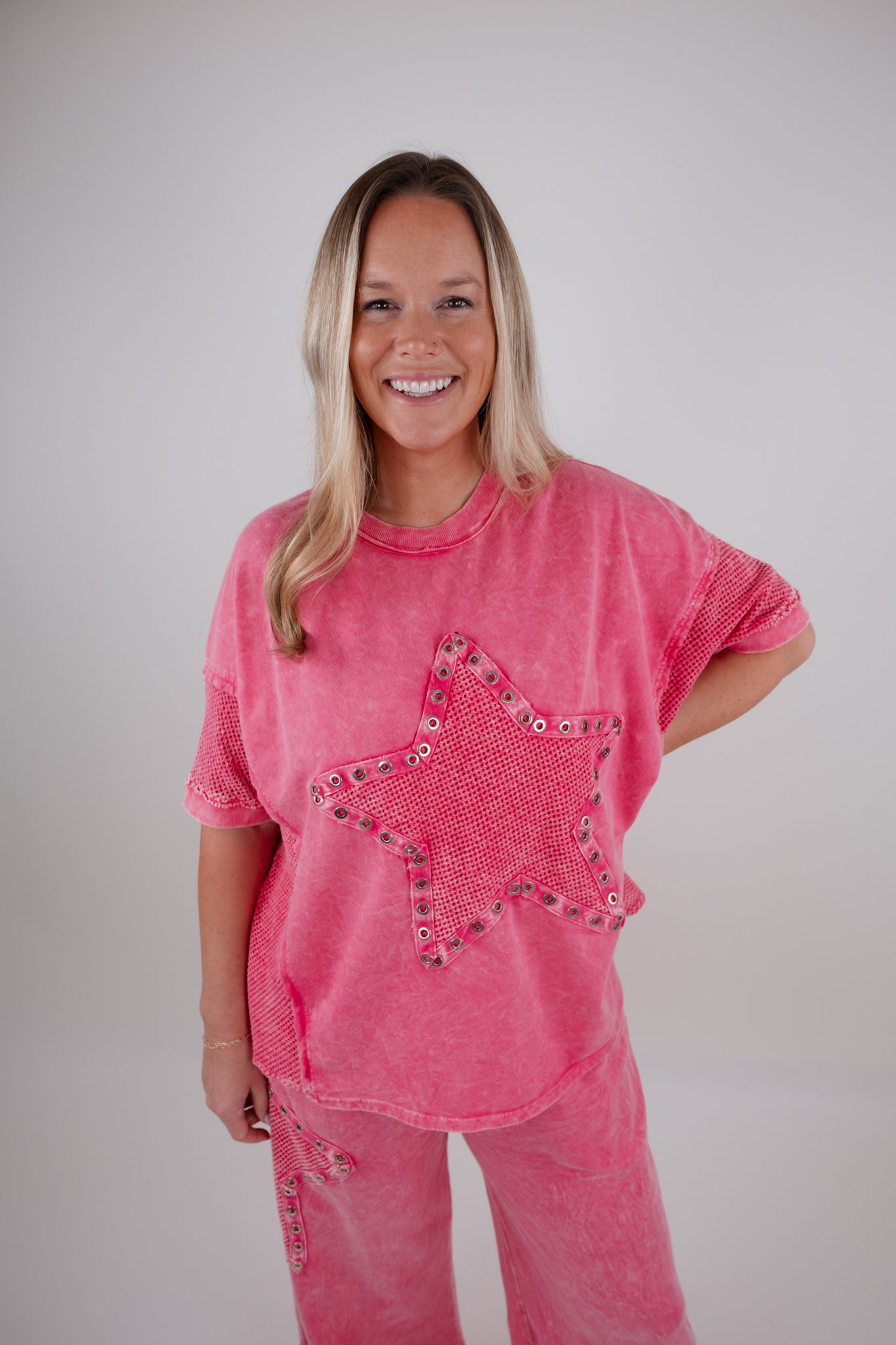 Woman wearing a pink distressed t-shirt with a star design on a plain background