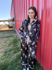 Woman wearing a black pajama set with horse print leaning against a red barn.