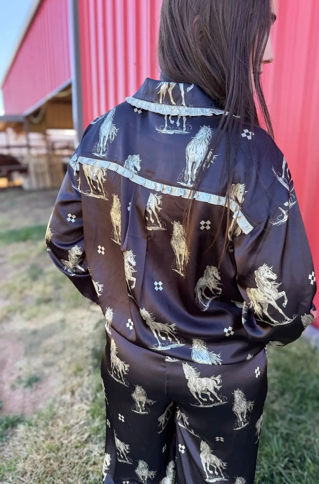 Person wearing a black pajama set with horse print in front of a red barn.