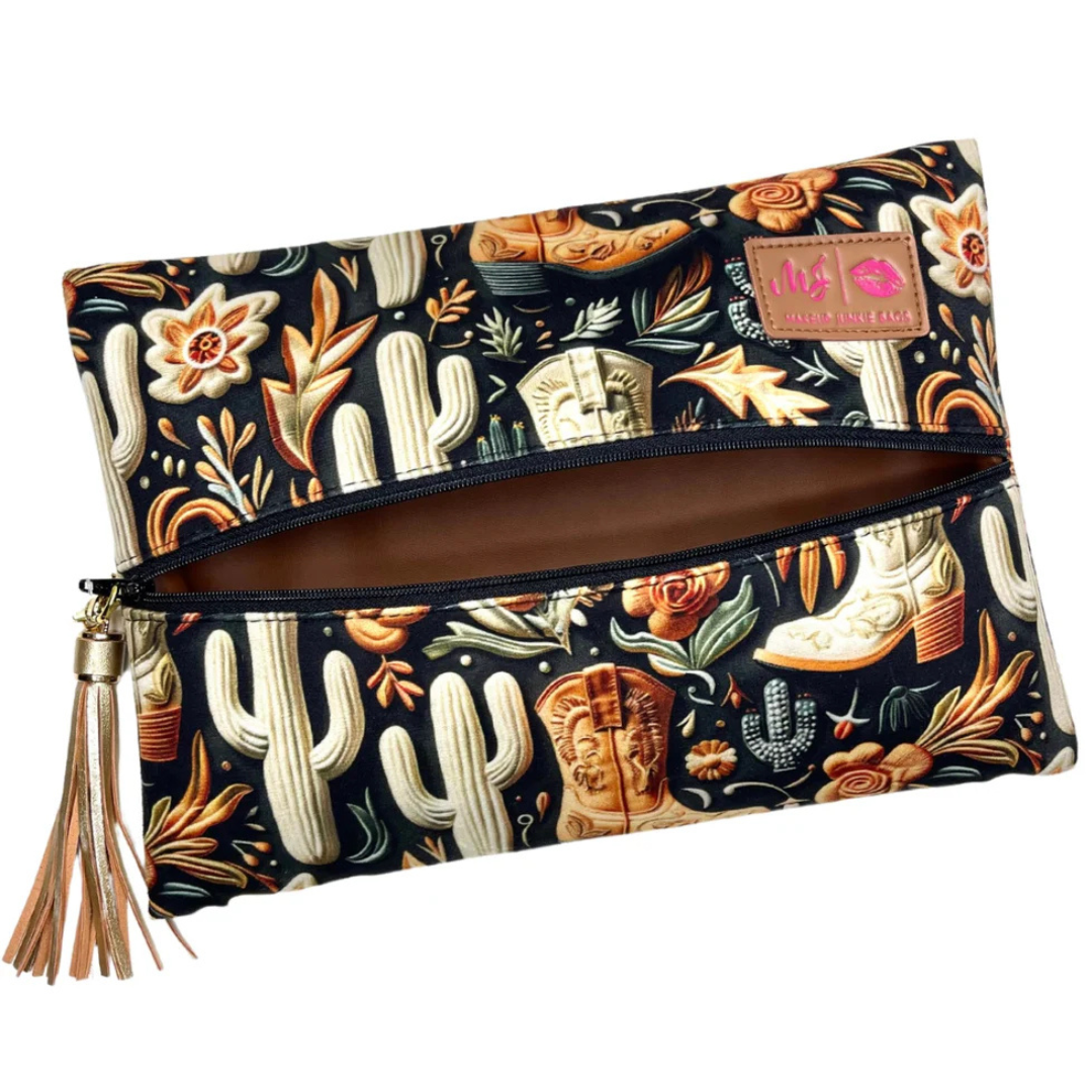 Front view of Boot Babe travel bag featuring chocolate‑brown western boot print on tan backdrop, black zipper and gold tassel pull.
