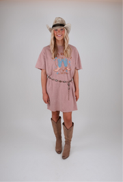 Woman wearing a pink dress with a graphic design, brown boots, and a cowboy hat on a white background