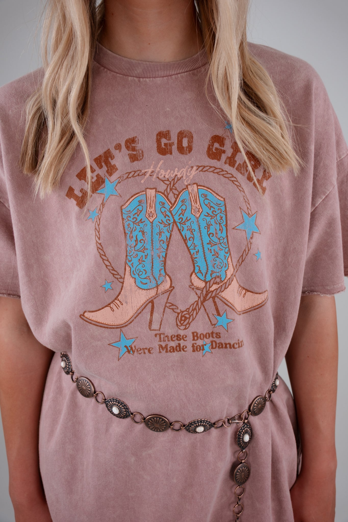 Person wearing a pink t-shirt with cowboy boot graphic and text.