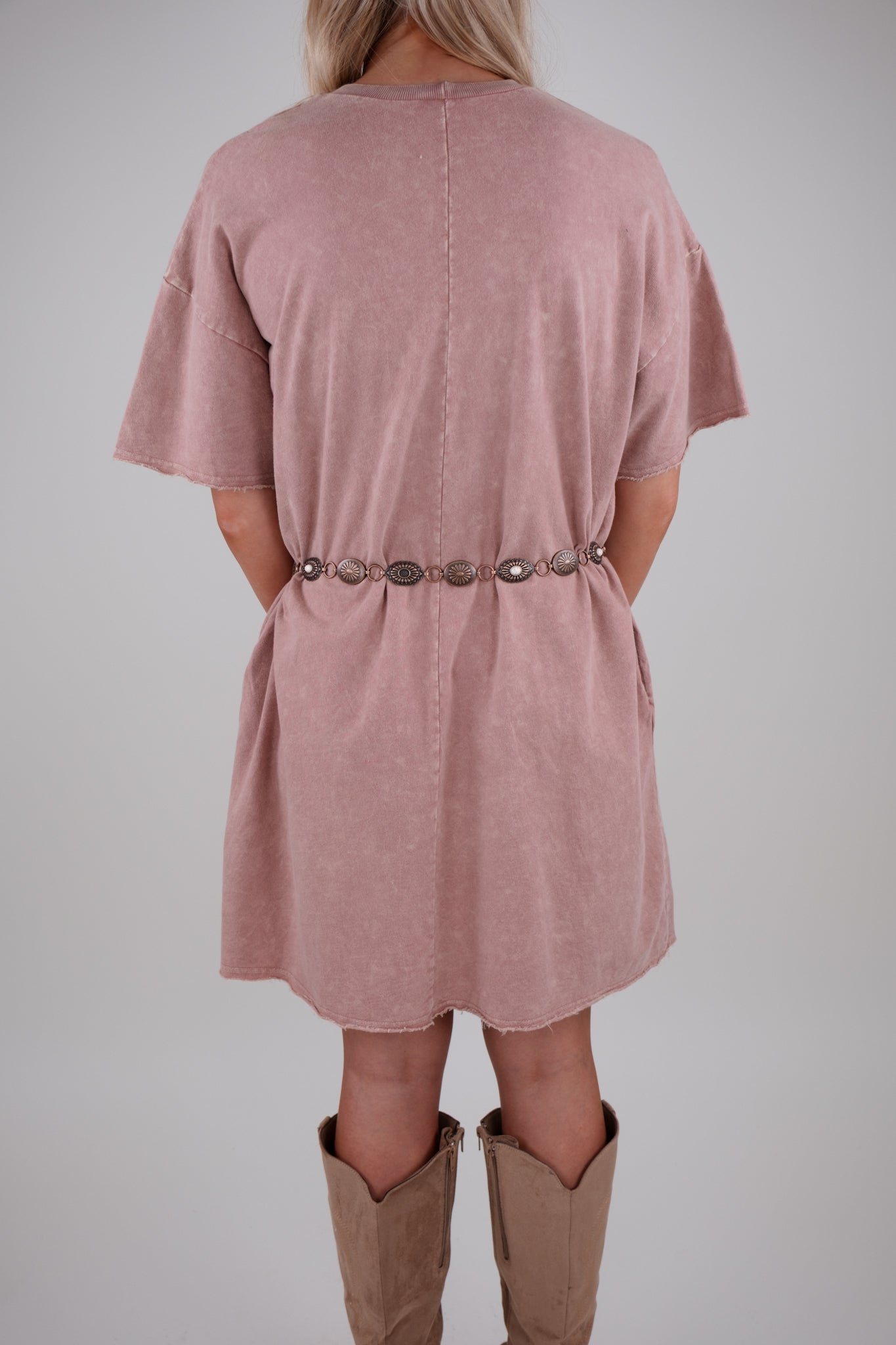 Person wearing a pink dress with a belt and brown boots on a plain background