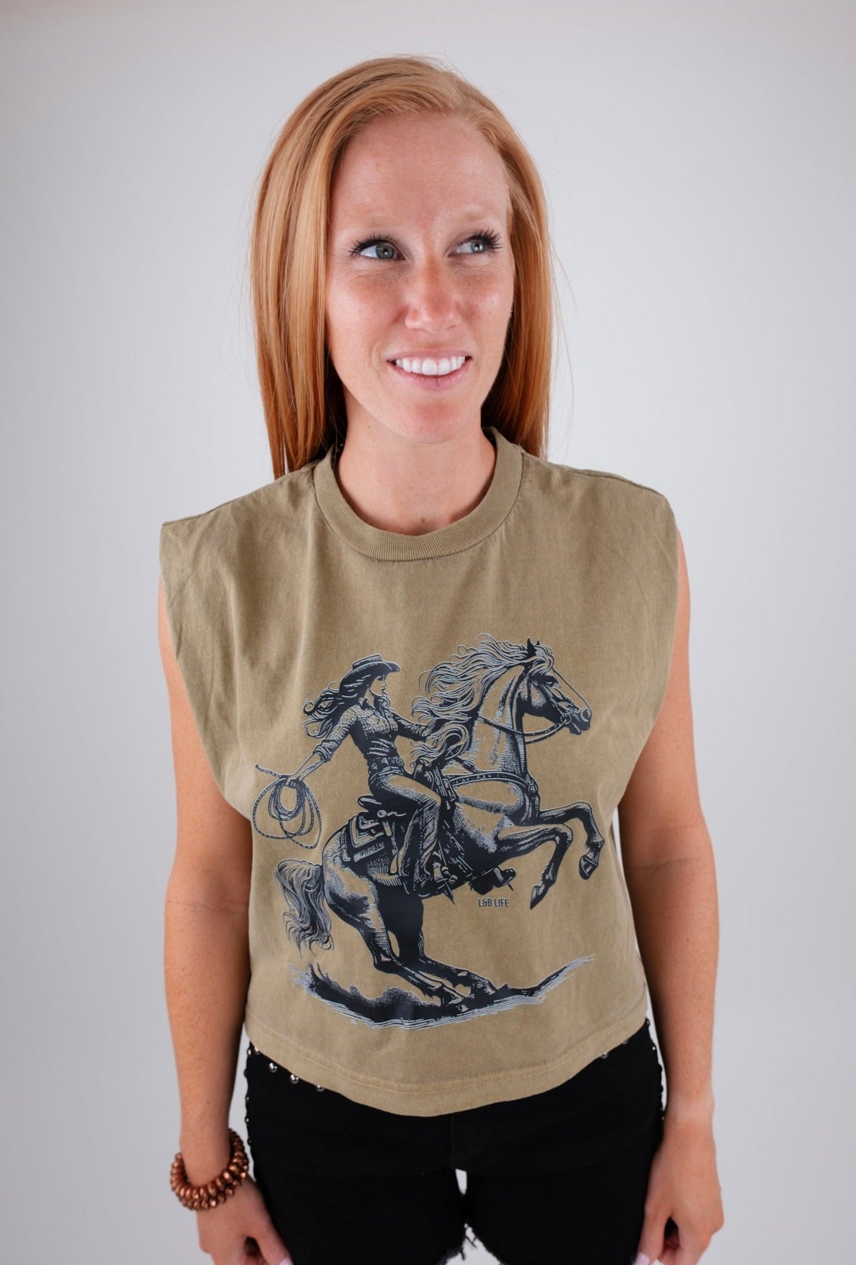 Woman wearing a sleeveless beige top with a graphic design of a person on horseback against a plain background