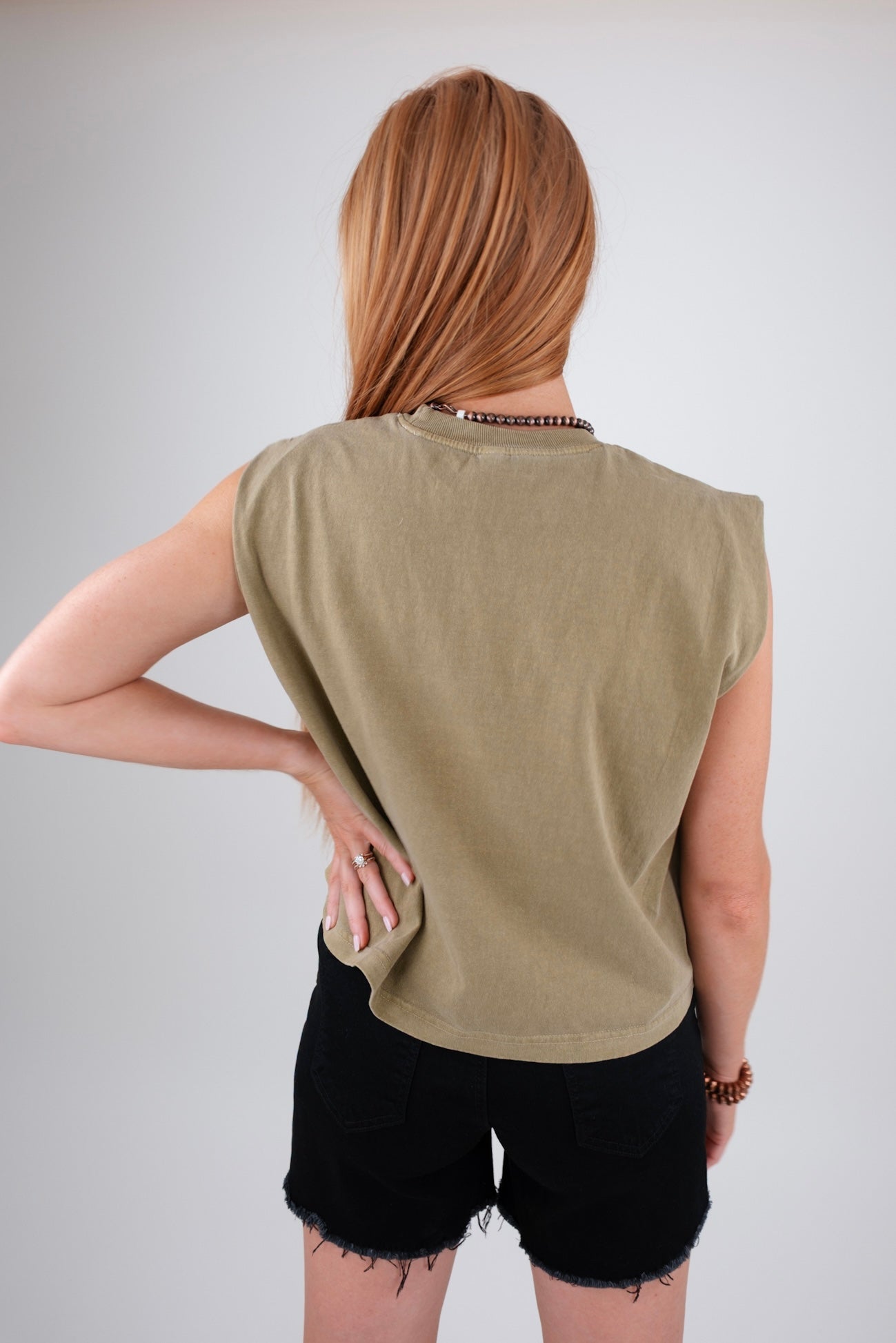 Person wearing an olive green sleeveless top and black shorts on a plain background