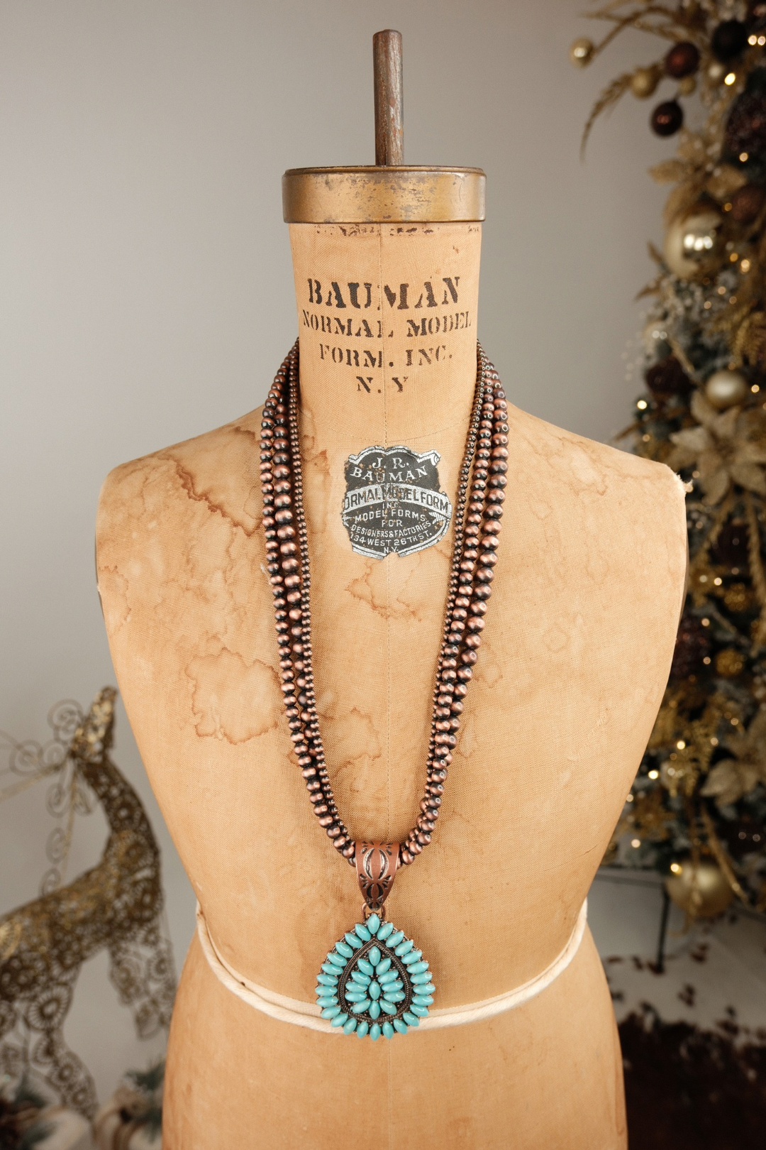 Necklace with a large turquoise pendant displayed on a mannequin bust with a vintage-style box labeled 'Bauman'.