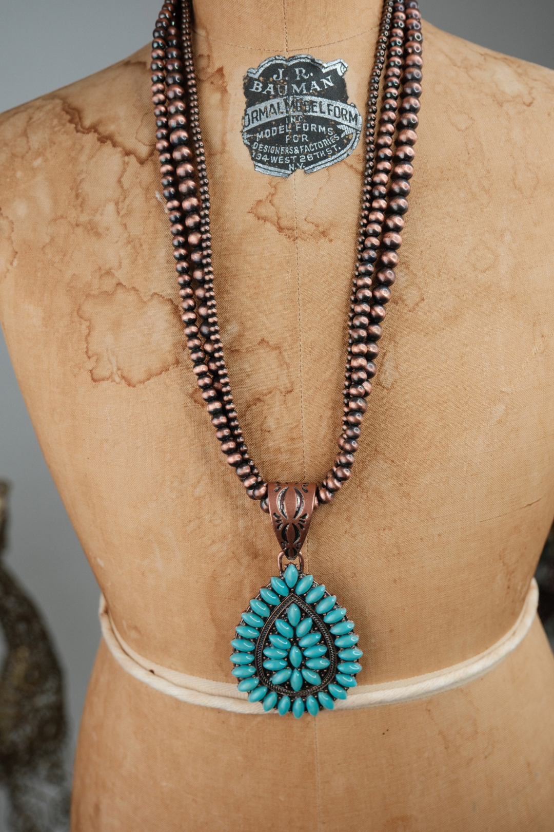 Necklace with turquoise pendant on a mannequin with visible brand label.