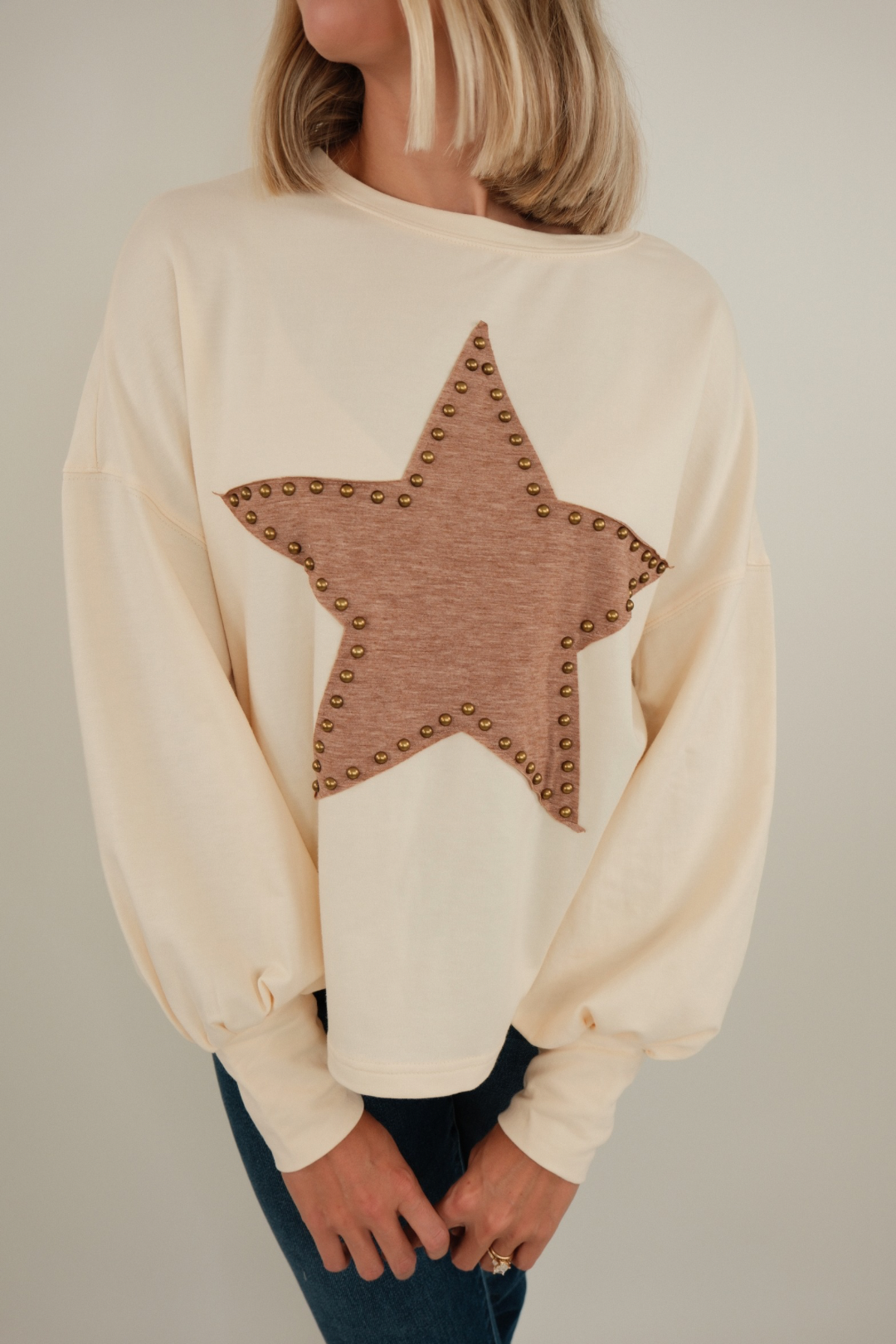 Front view of Bronze Star Pullover, cream knit sweater with brown star motifs, bronze studded embellishments, and relaxed western fit.
