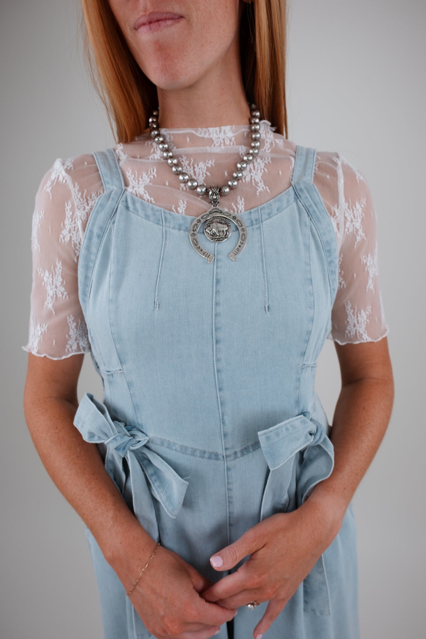 Person wearing a light blue denim dress with lace sleeves against a neutral background