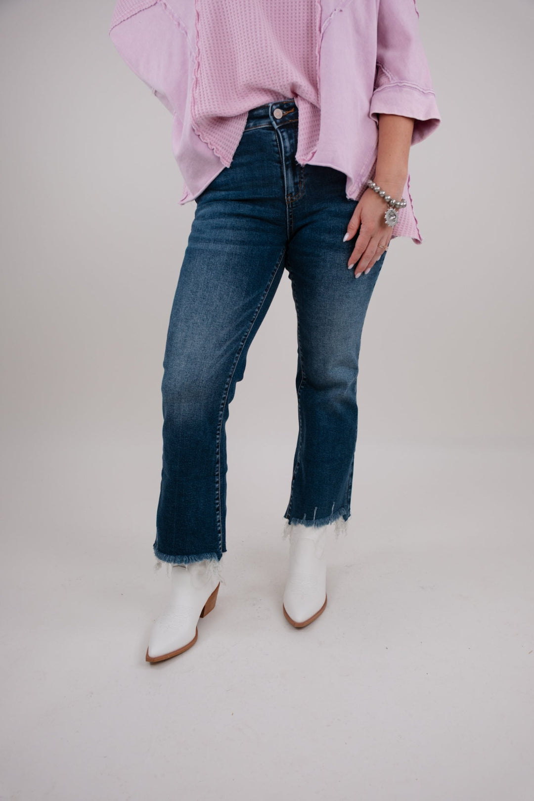 Person wearing a pink oversized shirt, blue jeans, and white ankle boots on a plain background