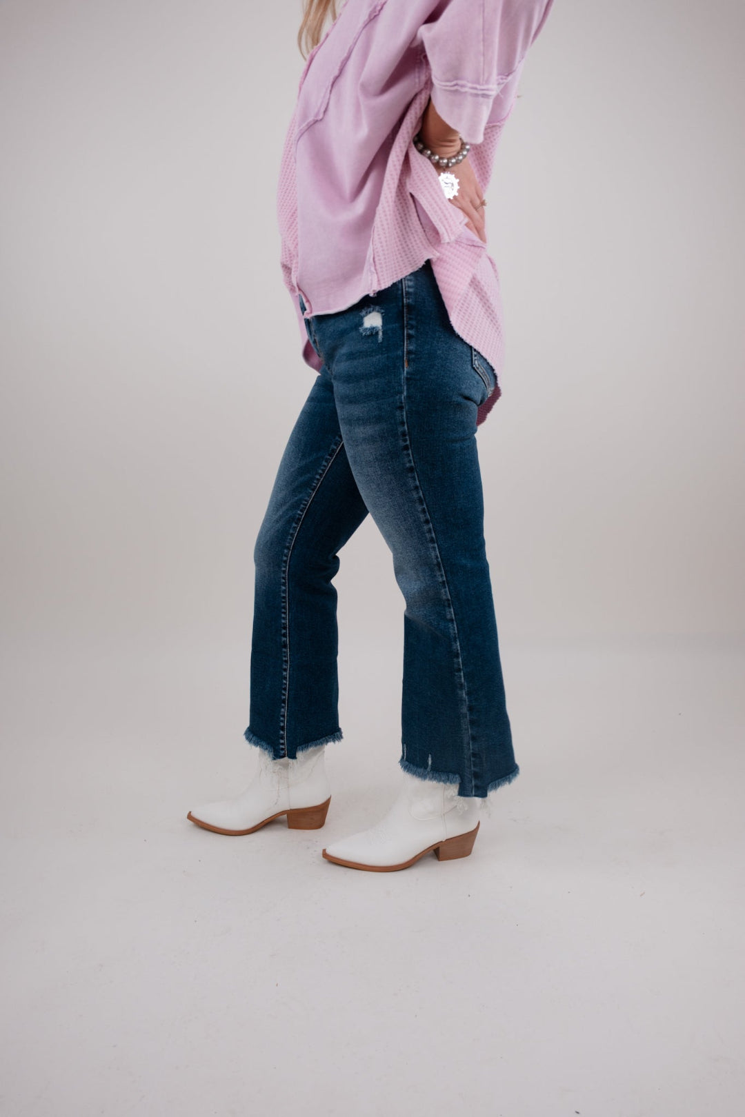 Person wearing a pink oversized shirt, blue jeans, and white boots on a plain background