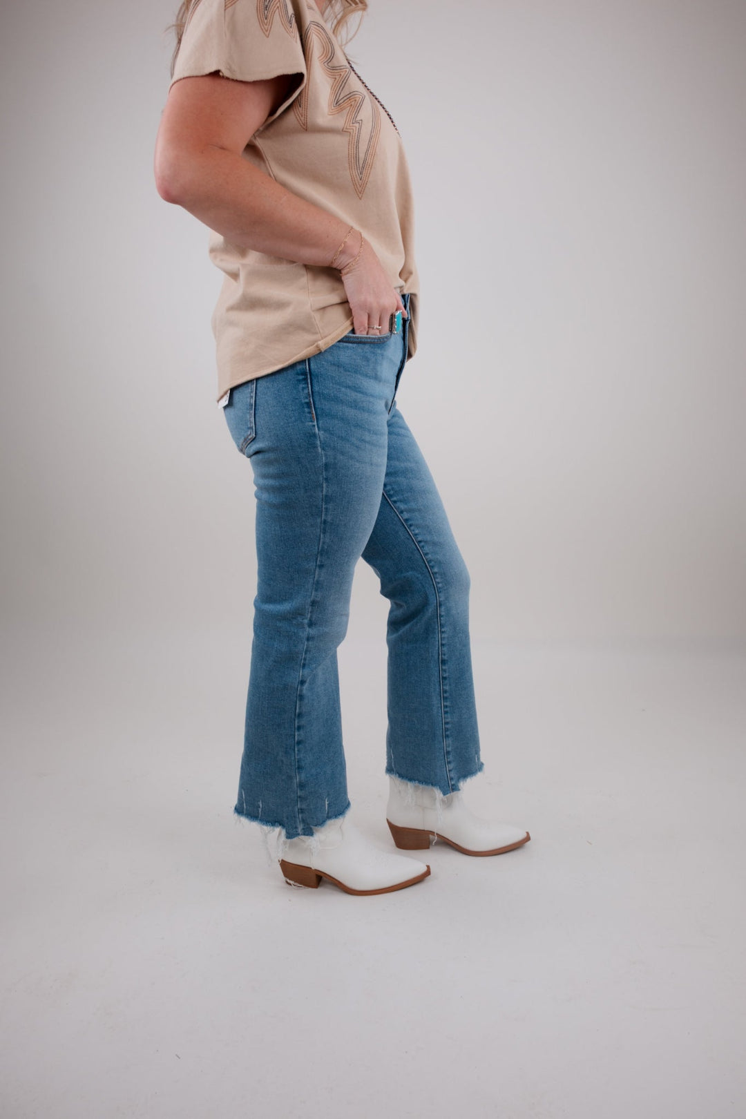 Person wearing a beige top, blue jeans, and white boots on a plain background