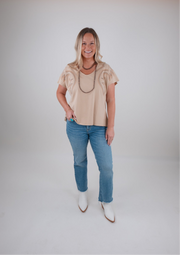 Woman wearing a beige top and blue jeans with white boots on a plain background