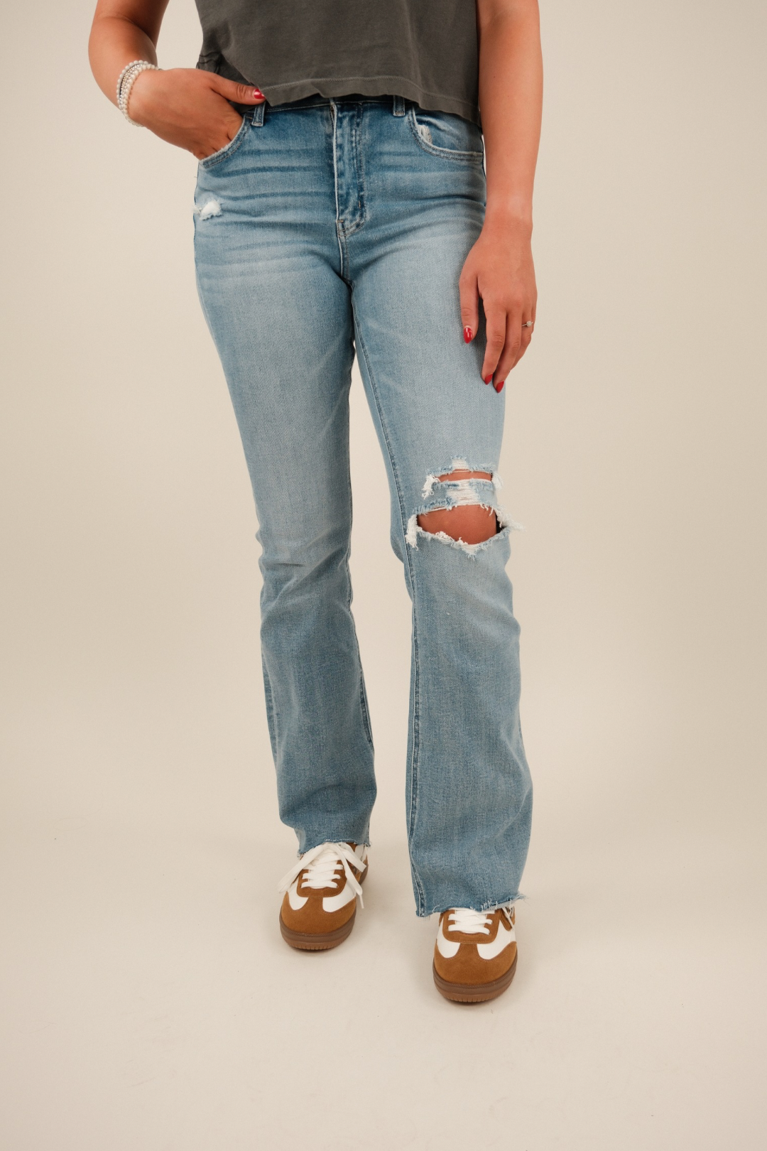 Model wearing light‑wash mid‑rise bootcut jeans with distressed knee, raw asymmetrical hem, and classic five‑pocket styling.