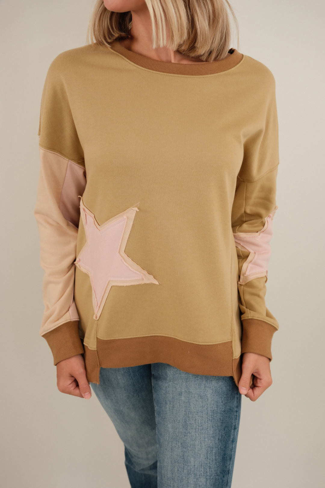 Close-up of Cosmic Cowgirl Pullover in tan highlighting bold star patches, contrast sleeve color block and soft textured knit.