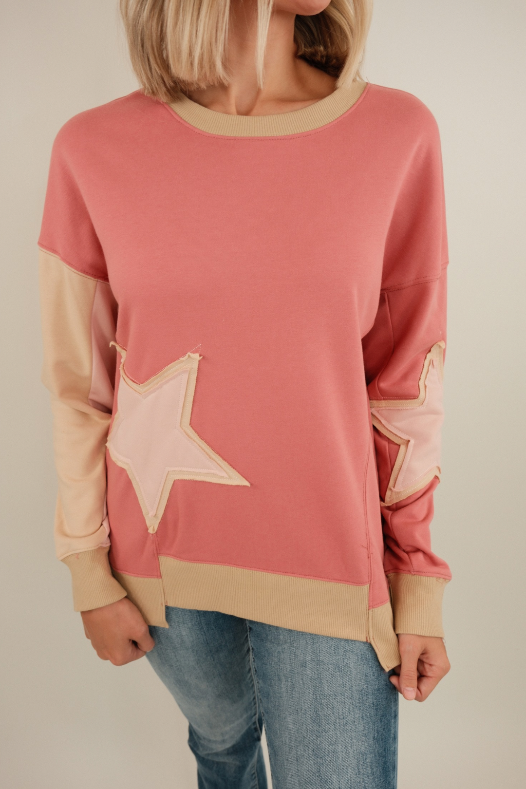 Close-up of Cosmic Cowgirl Pullover in rose highlighting bold star patches, contrast sleeve color block and soft textured knit.