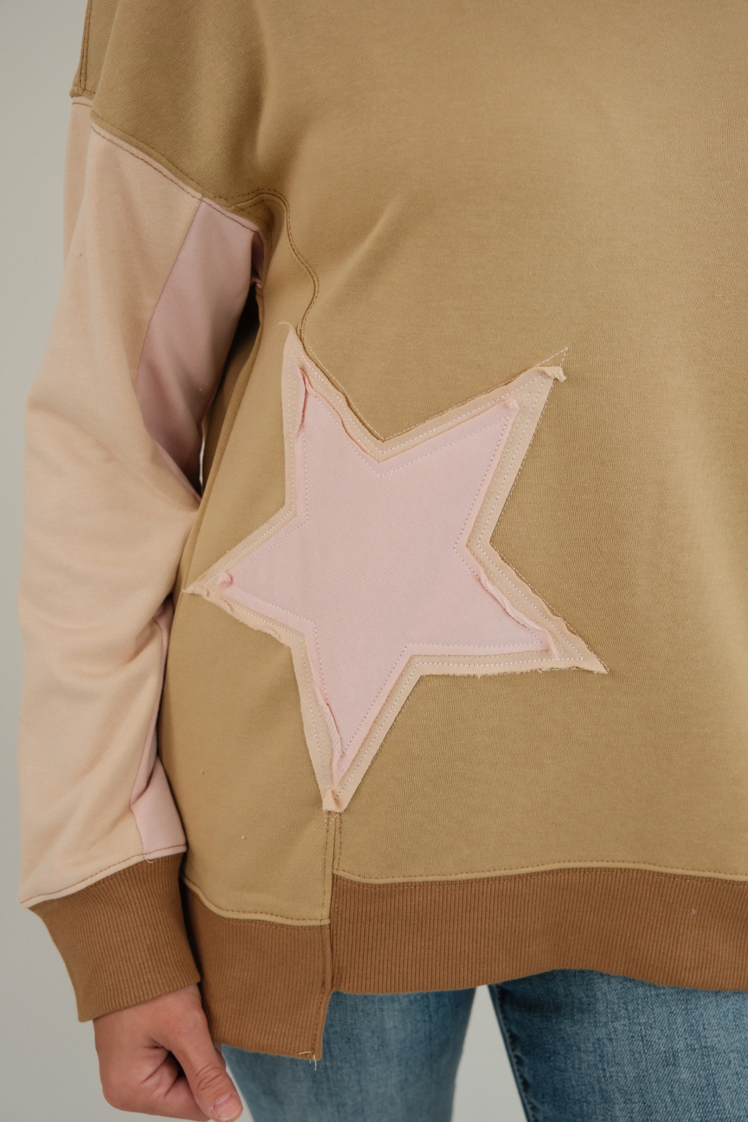 Close-up of women’s Cosmic Cowgirl Pullover in tan showing bold western star patches on chest and sleeve with soft knit fabric.