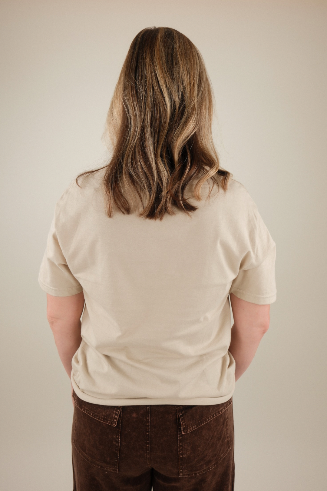 Person wearing a beige t-shirt and brown pants from behind on a plain background