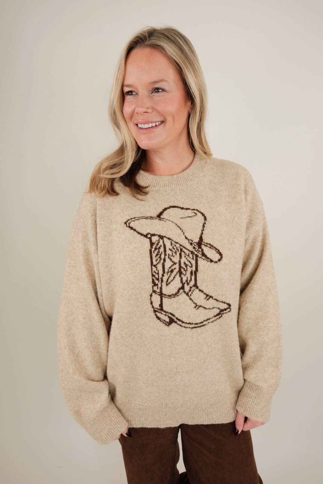 Front view of Cowgirl Classic Sweater, soft beige knit with brown cowboy hat and boot design, relaxed fit, and classic western style.