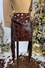 Brown leather handbag with fringe on a mannequin against a decorative background