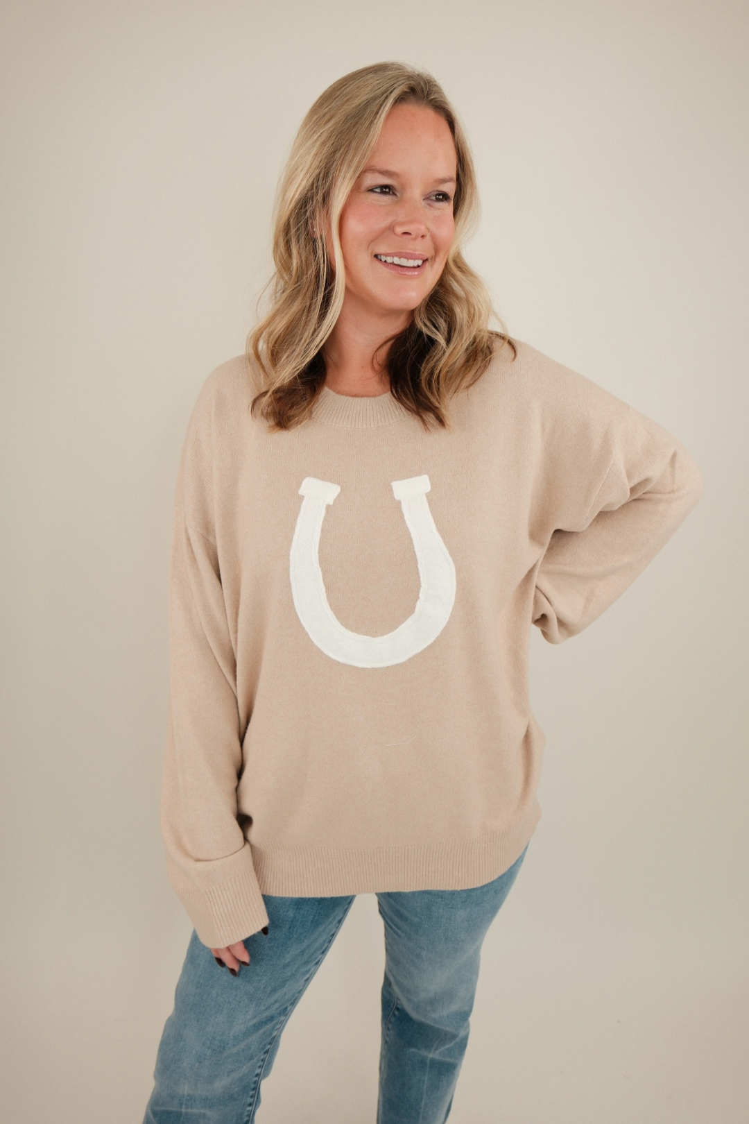 Front view of beige Cowgirl’s Luck Sweater, soft knit with cream horseshoe design and relaxed cowgirl fit for timeless western charm.