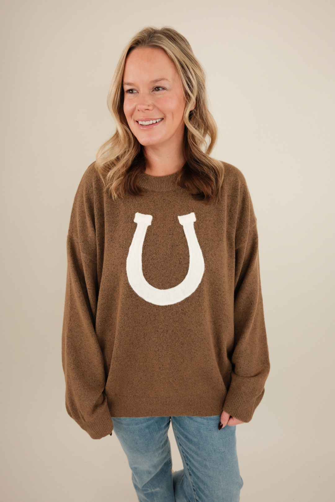 Front view of warm brown Cowgirl’s Luck Sweater, cozy knit with cream horseshoe design, relaxed fit, and rustic western style.