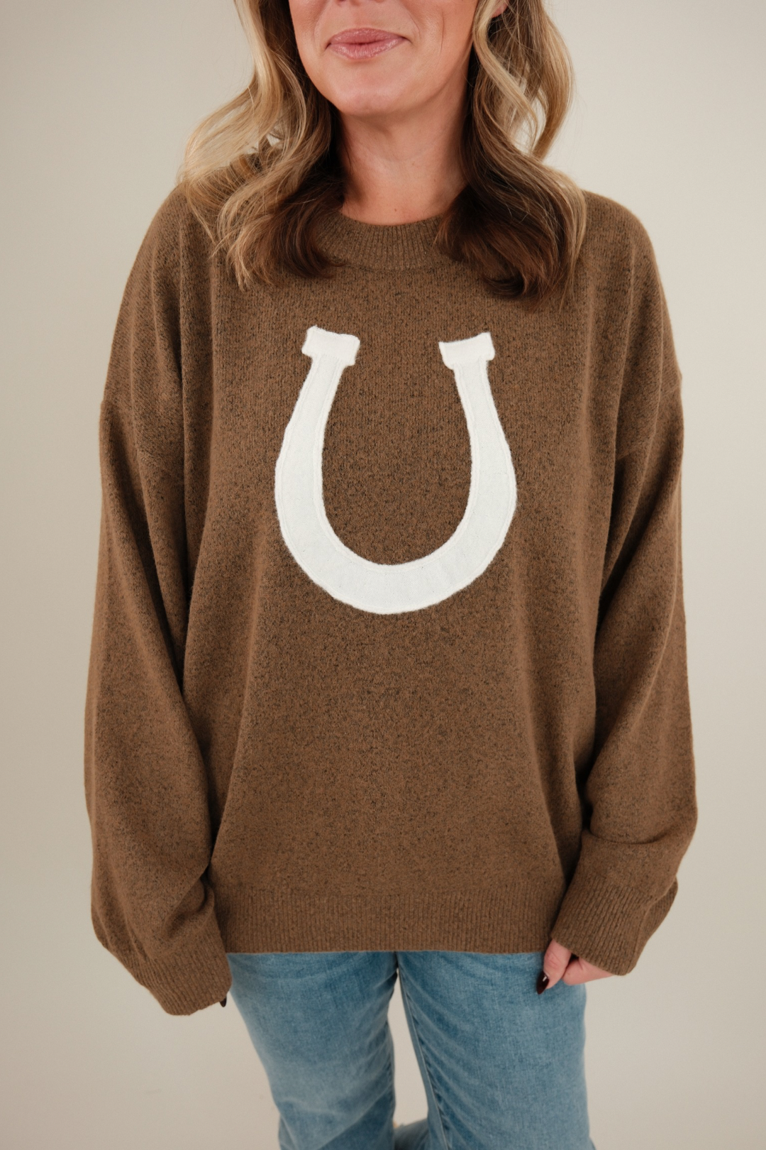 Model wearing warm brown Cowgirl’s Luck Sweater styled with denim, cozy knit pullover with cream horseshoe western detail.