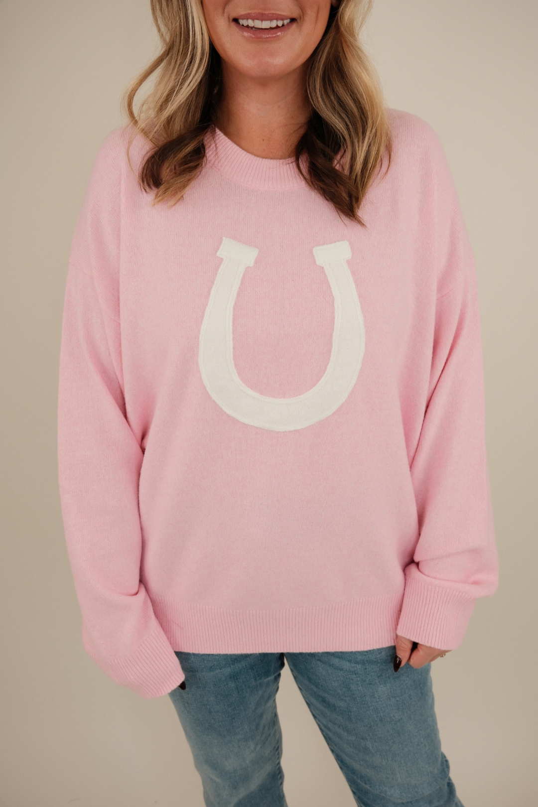 Full body shot of model in blush pink Cowgirl’s Luck Sweater, soft western pullover with cream horseshoe and warm feminine style.