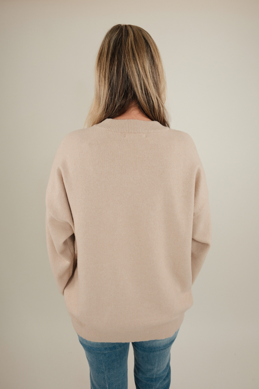 Back view of beige Cowgirl’s Luck Sweater showing cozy textured knit with cream horseshoe and relaxed neutral western style.