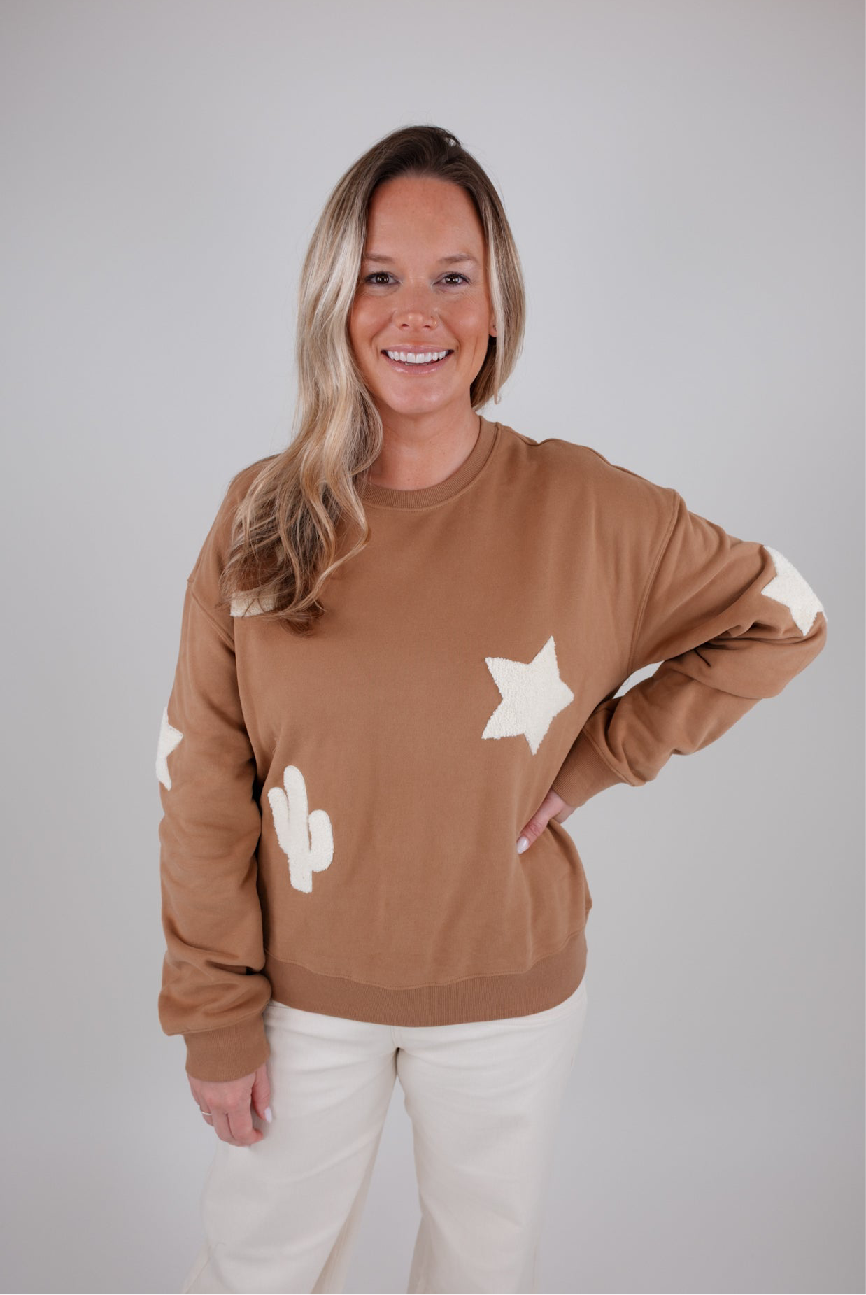 Woman wearing a brown sweatshirt with star and moon designs on a plain background