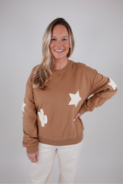 Woman wearing a brown sweatshirt with star and moon designs on a plain background