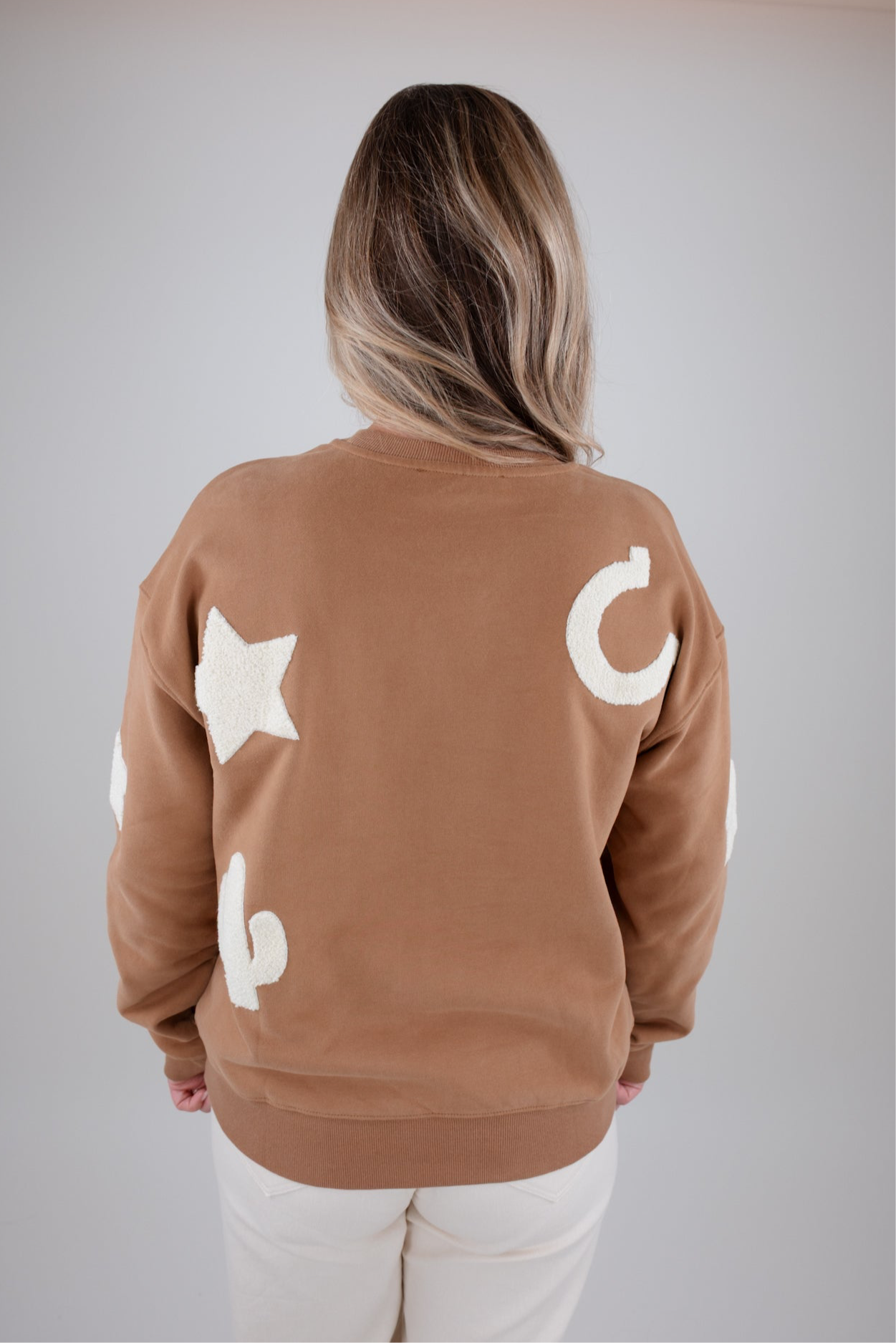 Person wearing a brown sweatshirt with white star and moon designs on a plain background