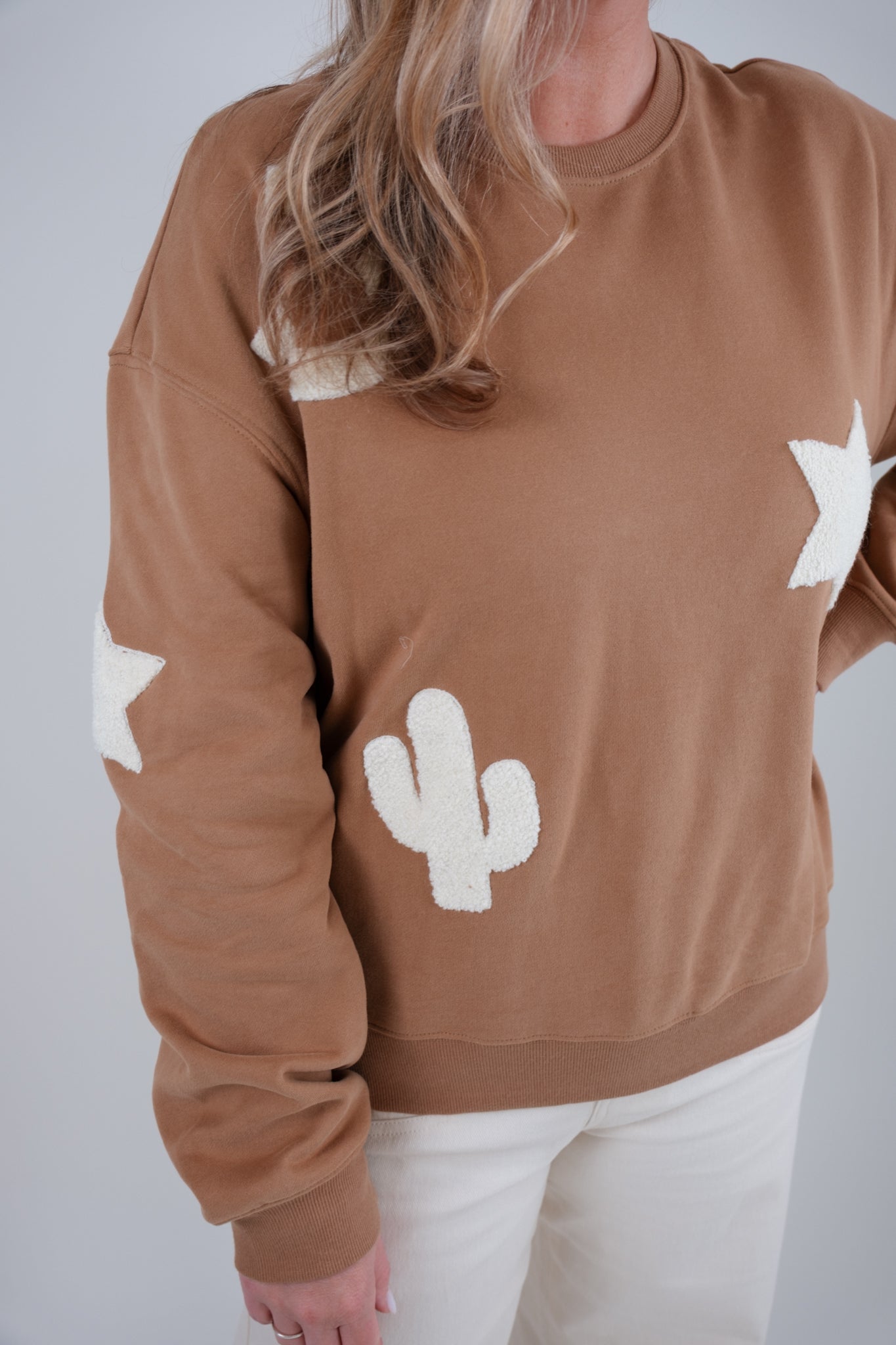 Brown sweatshirt with white star and cactus designs worn by a person on a plain background