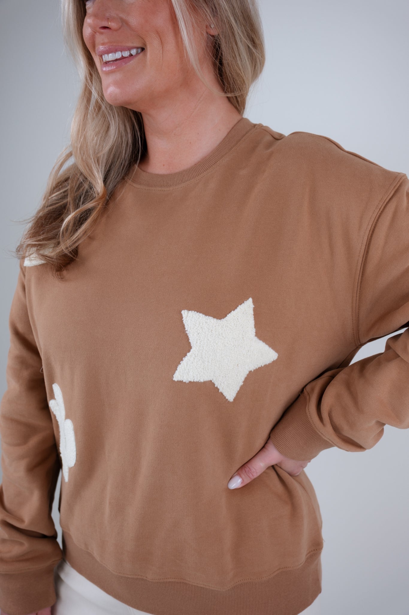 Woman wearing a brown sweatshirt with white star designs on a plain background