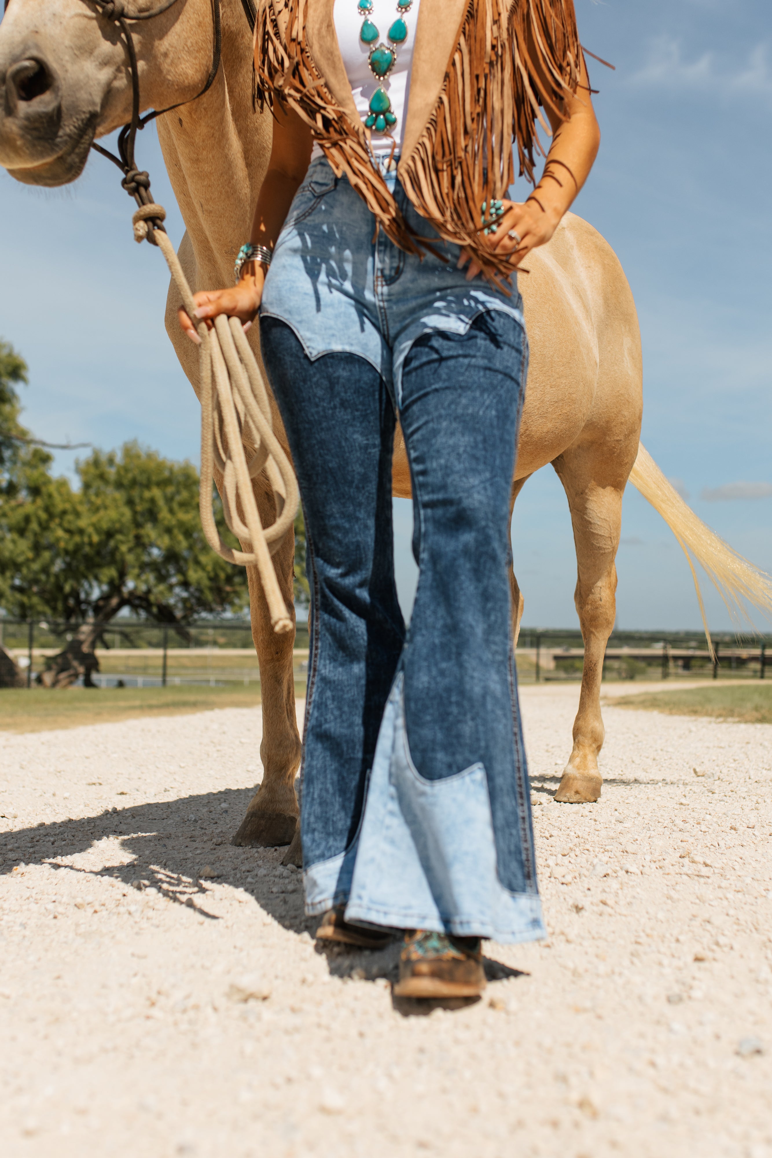 Person riding a horse wearing blue jeans with a fringed jacket.