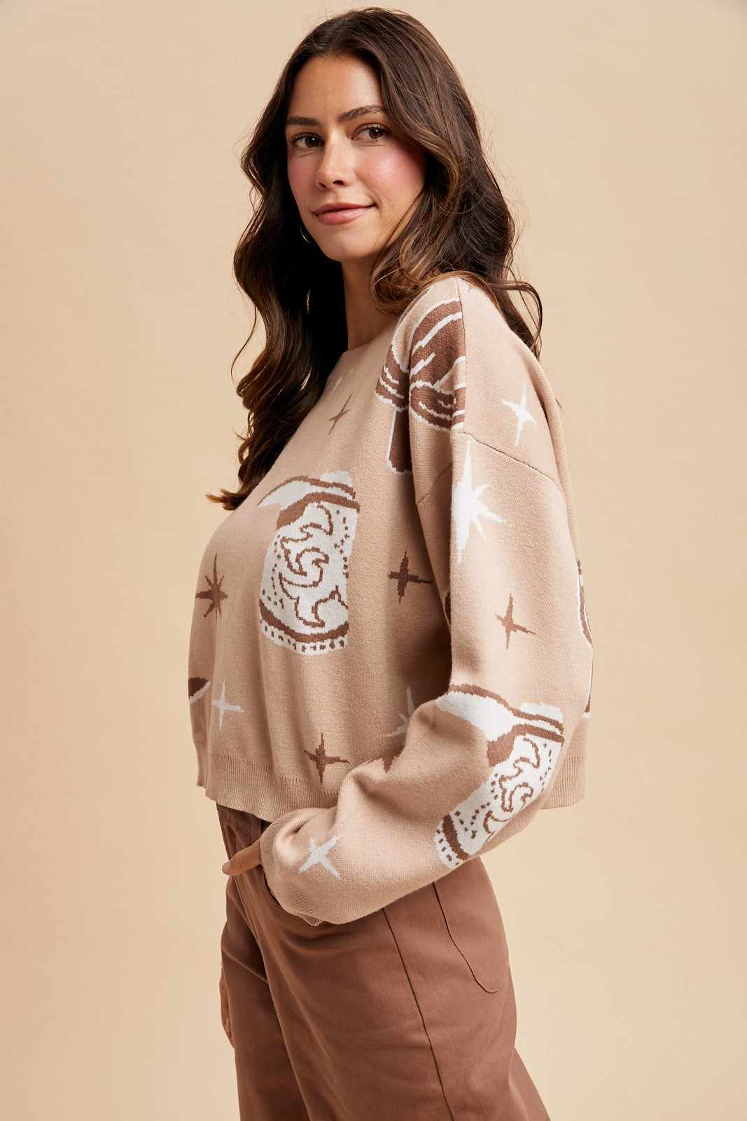 Woman wearing a beige sweater with star and pattern designs on a beige background
