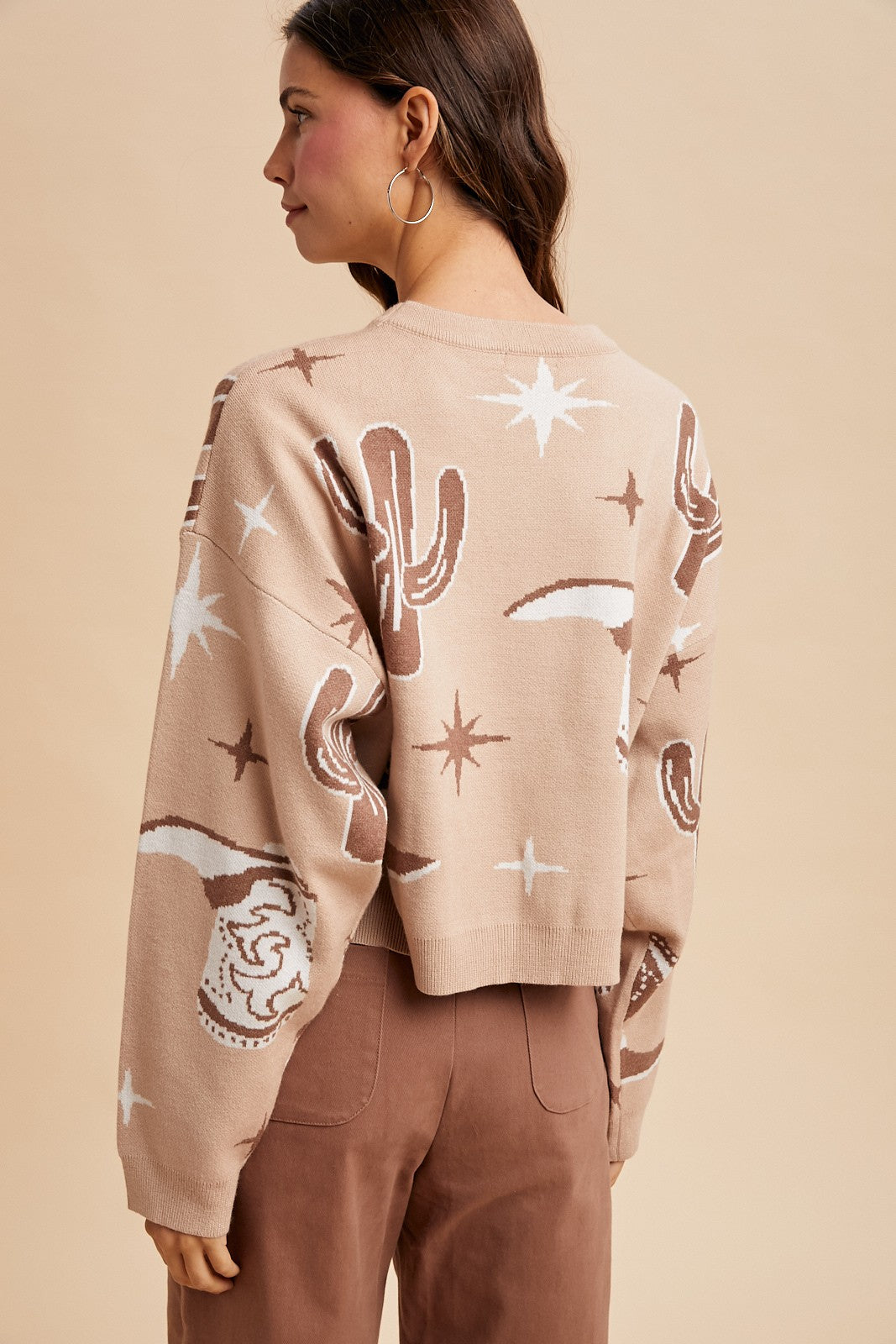 Woman wearing a beige sweater with cactus, boot, and star patterns on a beige background