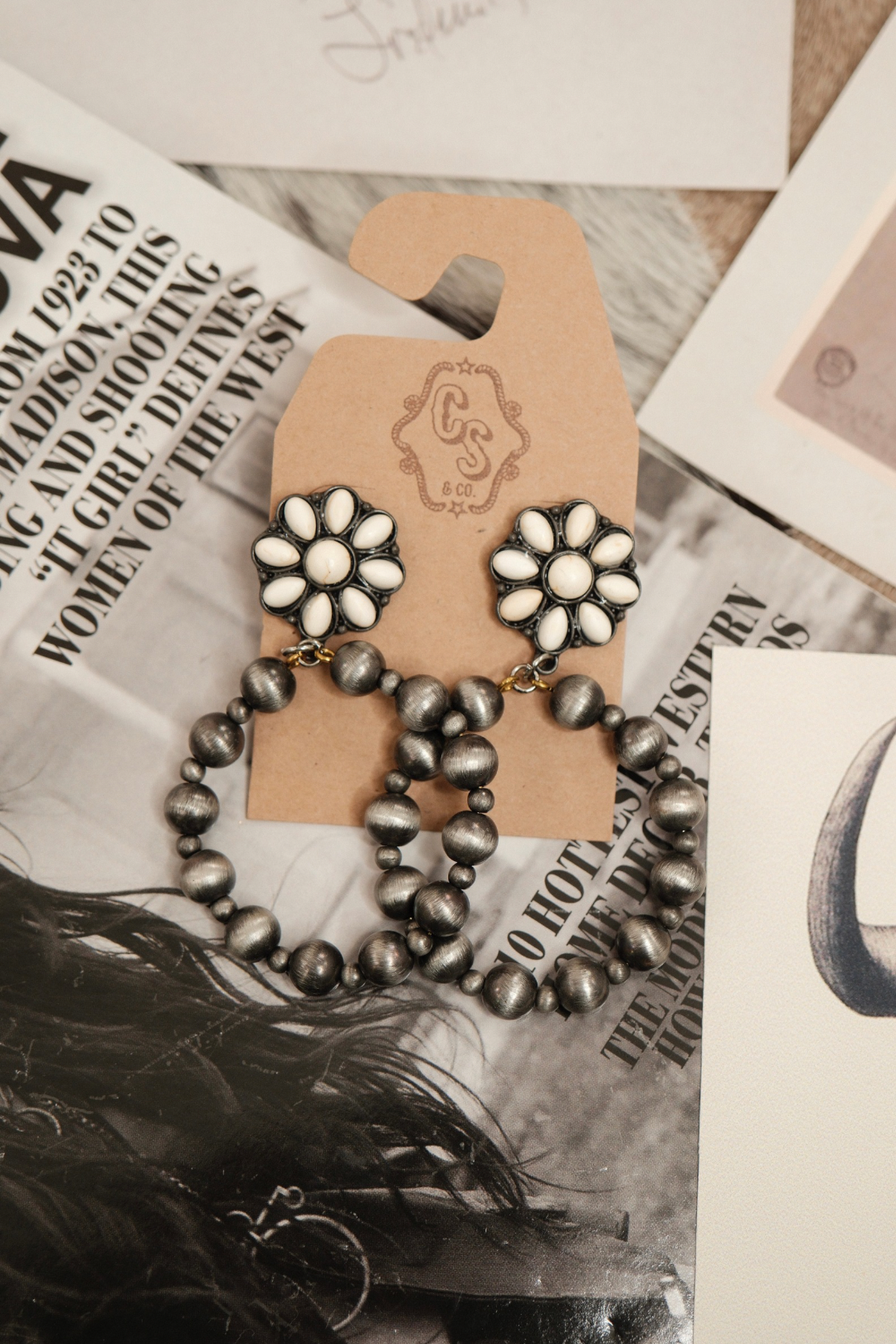 Floral earrings on a brown card with feathers and newspaper in the background