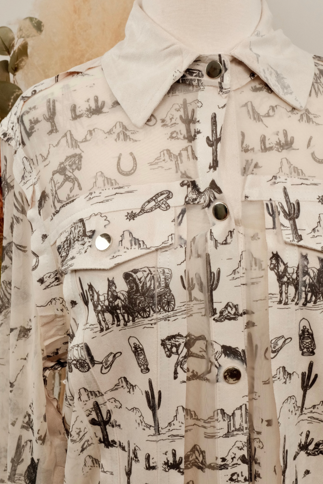 Close-up of a shirt with a desert-themed pattern featuring cacti, horses, and wagons.